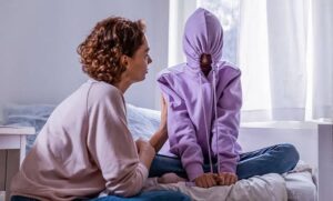 Person sat with hoodie over his face being supported by an adult