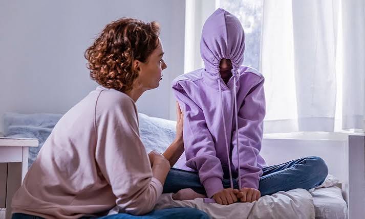 Person sat with hoodie over his face being supported by an adult